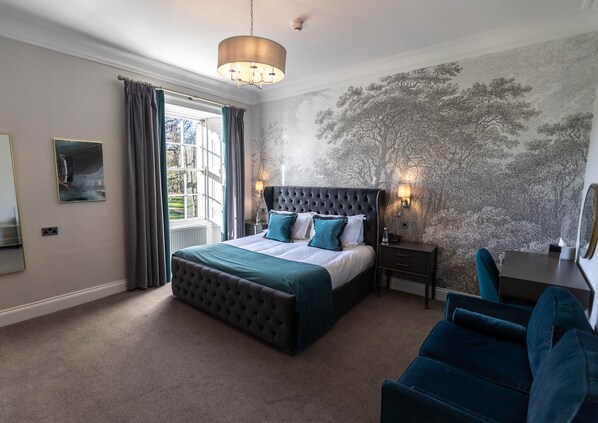 A bedroom with a large bed, a desk, and a chair. There is a window with curtains, a lamp, and a wall with a tree pattern. - Marshall Meadows Manor House (Berwick-upon-Tweed)