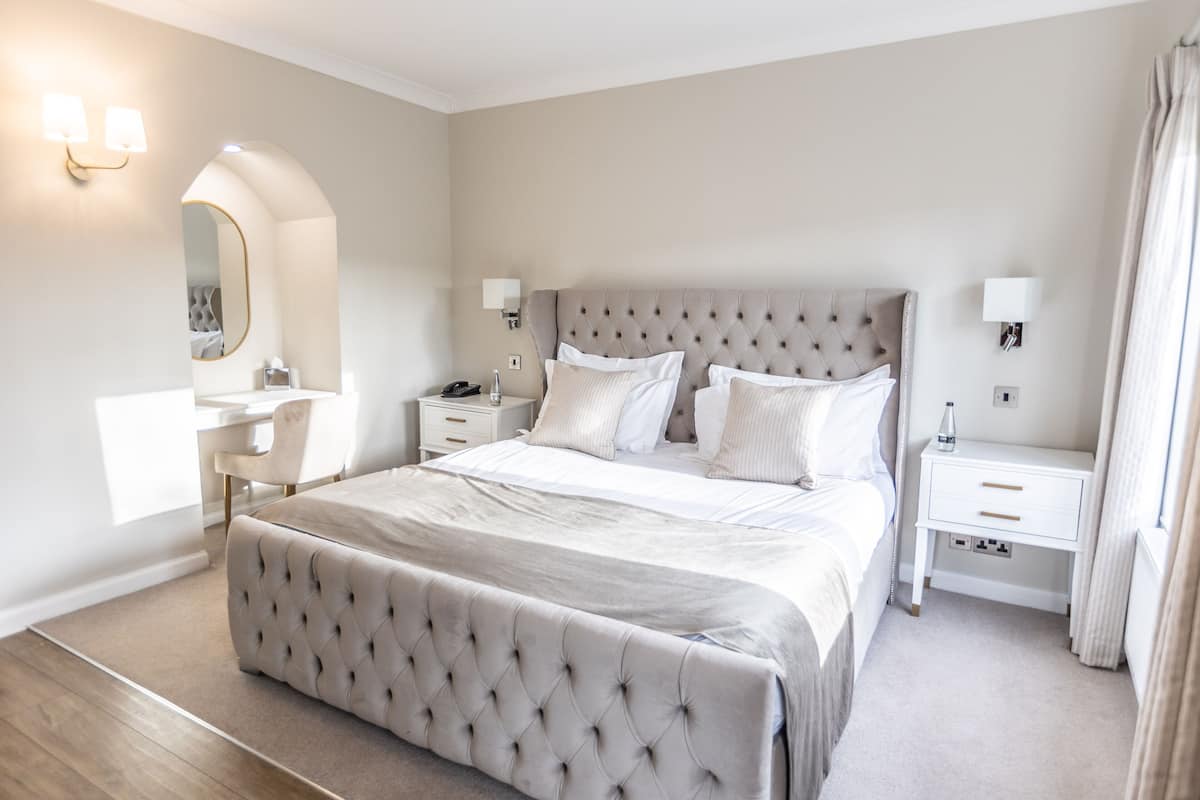 A modern bedroom with a tufted headboard, a bedside table with a lamp, and a large mirror.