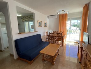 Ein Wohnzimmer mit Sofa, Esstisch, Stühlen, einem Fernseher und einer Küchenzeile mit Kühlschrank.