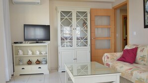 Een woonkamer met een televisie, een glazen salontafel, een bank met bloemenprint en een kast met glazen deuren.
