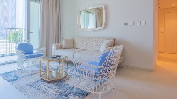 A modern living room with a white sofa, two white wicker chairs, a glass coffee table, and a large mirror on the wall. - Bellavista- Downtown View II - Burj View (Dubai)