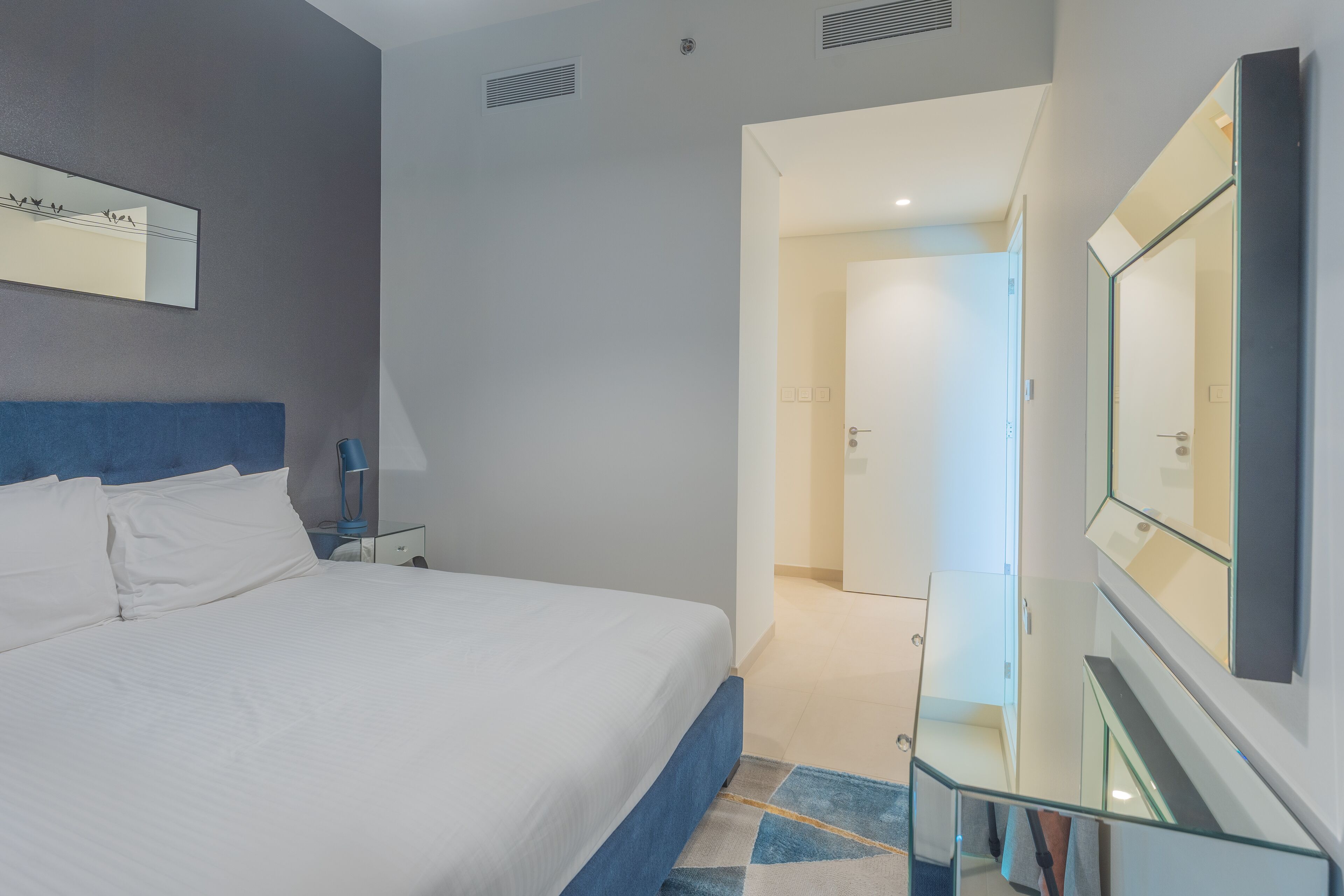 A modern hotel room with a large bed, a nightstand, a lamp, and a glass railing leading to a staircase.