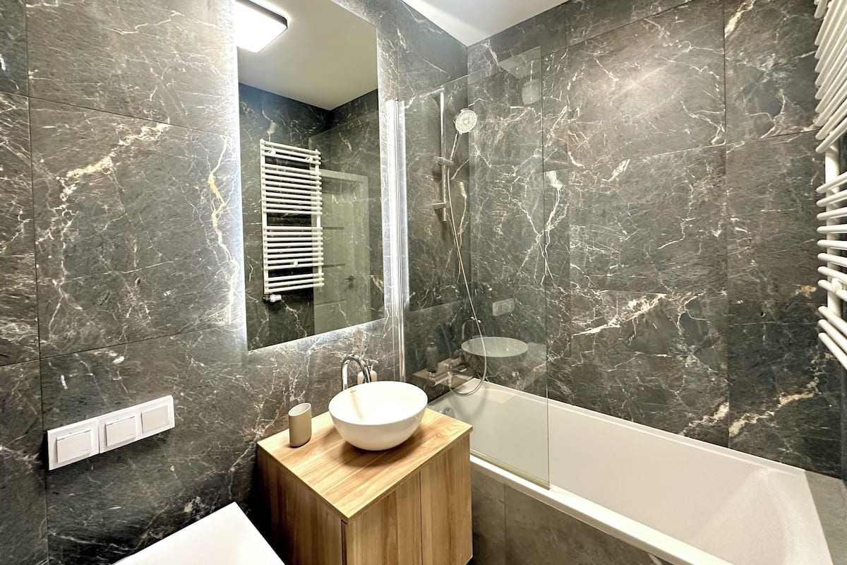 Ein modernes Badezimmer mit einem großen Spiegel, einem Holzwaschtisch, einem weißen Waschbecken und einer Badewanne.