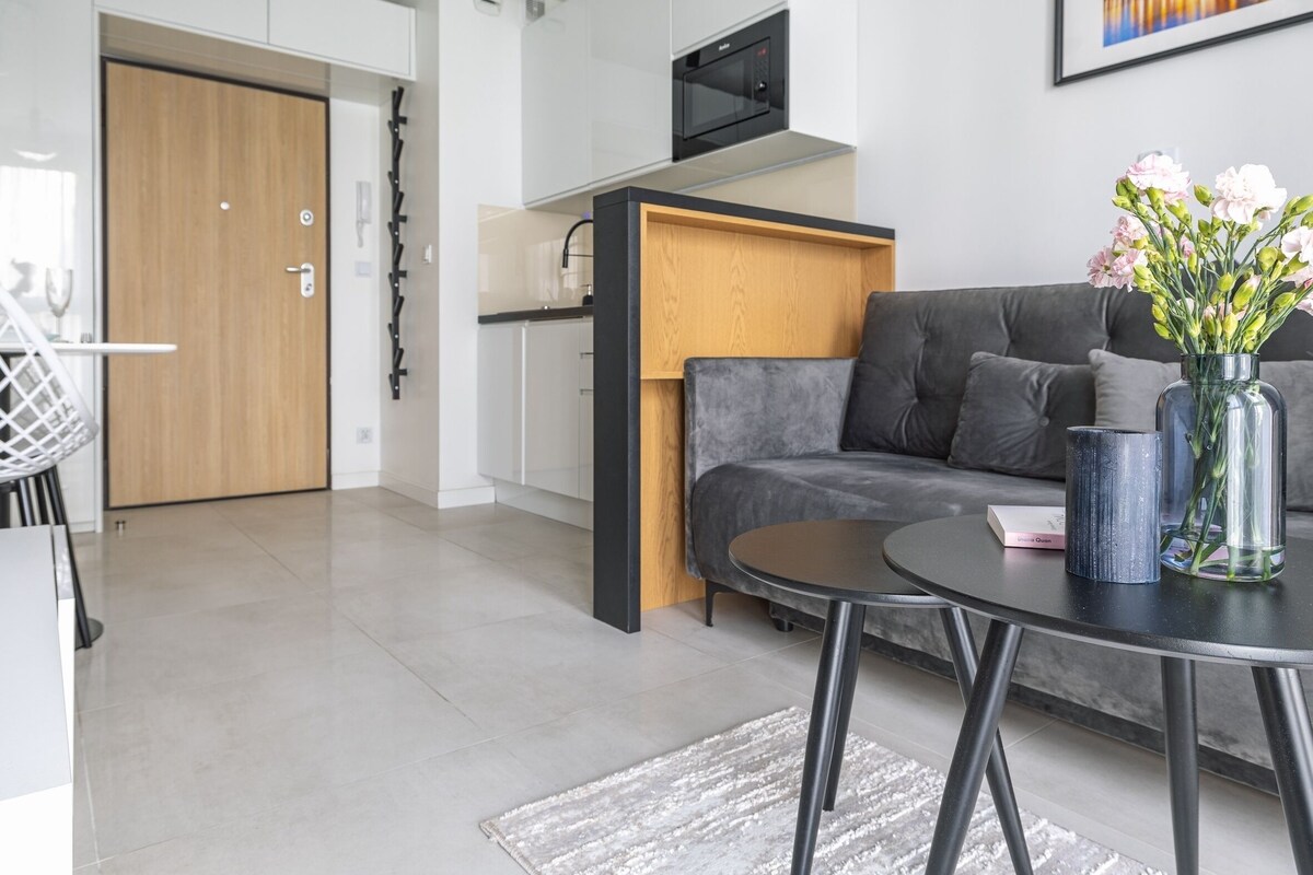 Een moderne woonkamer met een grijze bank, een ronde zwarte tafel en een vaas met bloemen.