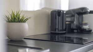 A modern kitchen with a black countertop, a white pot with green plants, and a coffee maker. - Aura 40 by Q4 Apartments (Gdansk)