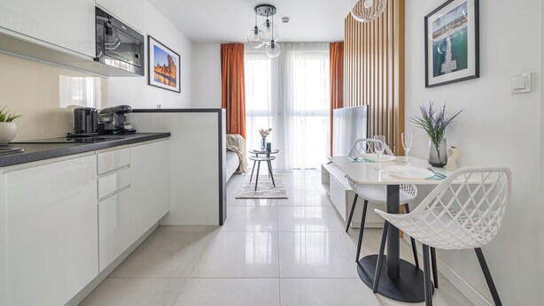 A modern kitchen with white cabinets, a black countertop, and a dining area with a white table and chairs. - Aura 40 by Q4 Apartments (Gdansk)