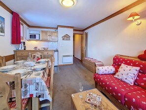 Uma sala de estar acolhedora com um sofá vermelho, um espaço de refeições com uma mesa posta para quatro pessoas e uma cozinha ao fundo.