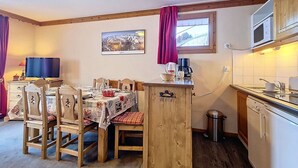 A cozy dining area with a wooden table and chairs, a small kitchen with a microwave, and a window with curtains.