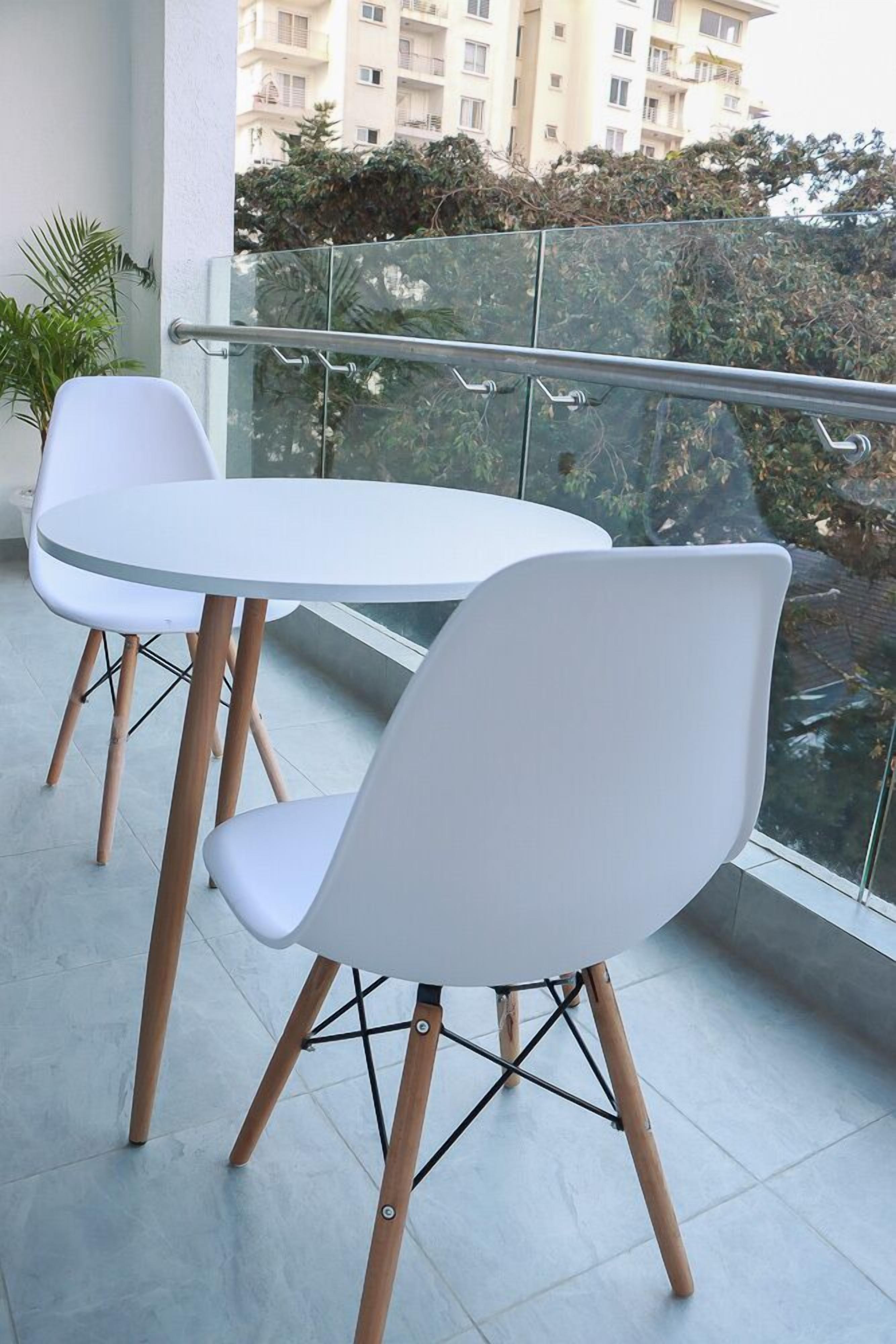A balcony with a white table and two white chairs, a potted plant, and a view of a residential building.