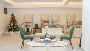 Un salon moderne avec une table basse ronde blanche, deux fauteuils verts à revêtement, un sapin de Noël et une grande fenêtre donnant sur la ville.