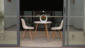 Une chambre moderne dotée d’une porte vitrée donnant sur un balcon, où l’on trouve une table ronde avec deux chaises blanches et une plante en pot.