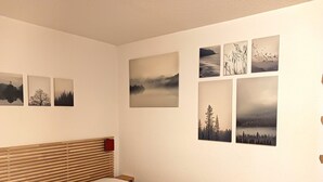Une chambre à coucher avec une tête de lit en bois, un lit recouvert d’un drap blanc et six photographies de paysages accrochées au mur.