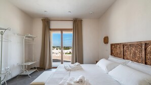 A hotel room with a bed, a window with curtains, a view of the beach, and a wooden headboard.
