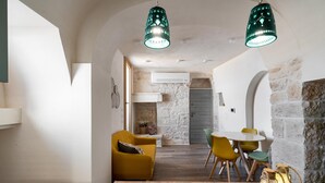 A cozy interior with a stone wall, a yellow sofa, a round table, and two hanging green lamps.
