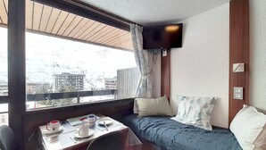 A compact room with a bed, a small table with a chair, a TV mounted on the wall, and a window overlooking a cityscape. - Renovated studio for 3, south-west balcony, ski-in/ski-out (Les Menuires)