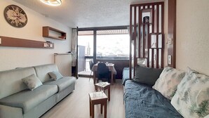 A living room with a grey sofa, a blue sofa, a small wooden table with glasses, and a clock on the wall. - Renovated studio for 3, south-west balcony, ski-in/ski-out (Les Menuires)
