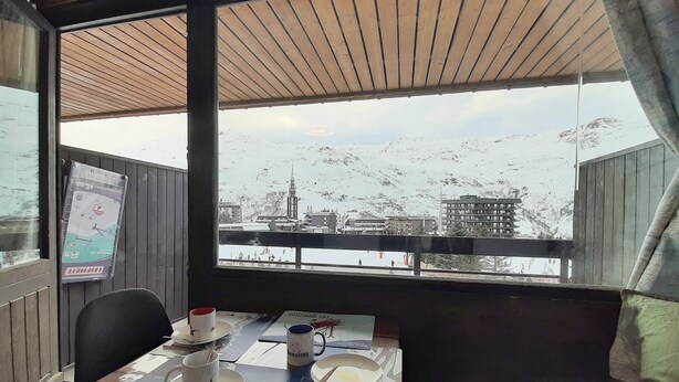 A table set with a cup, saucer, and a plate, with a window view of a snowy landscape and buildings. - Renovated studio for 3, south-west balcony, ski-in/ski-out (Les Menuires)