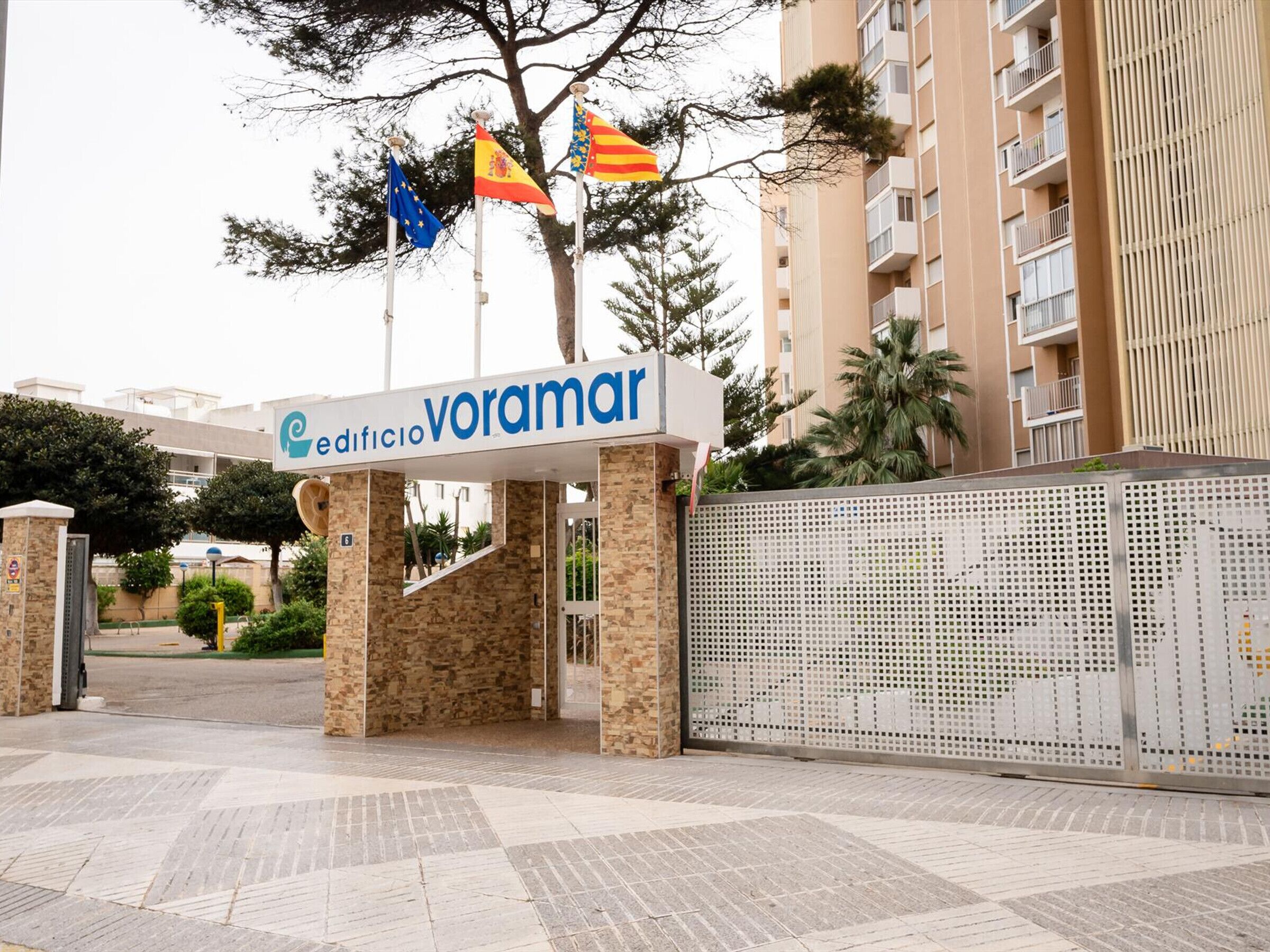 Ein Gebäudeeingang mit einem Schild, auf dem 'edificio voramar' steht, und Flaggen Spaniens, der EU und Kataloniens.