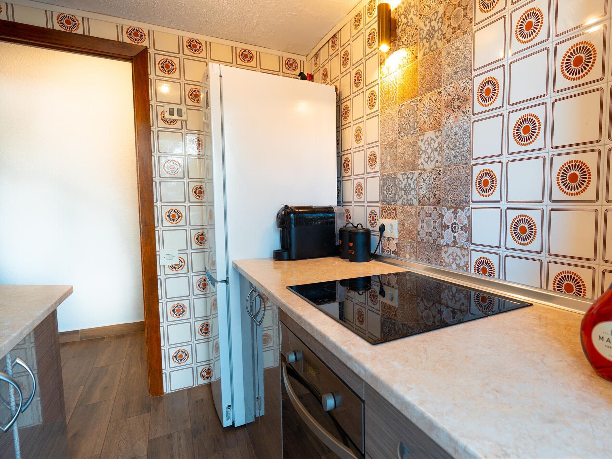 A compact kitchen with a built-in stove, a refrigerator, and a coffee machine.