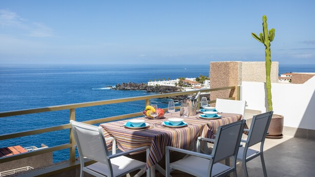 A dining table set for two with a view of the sea, a cactus plant, and a stone wall. - Our Ocean Penthouse, luxury, views y relax ! (Guía de Isora)