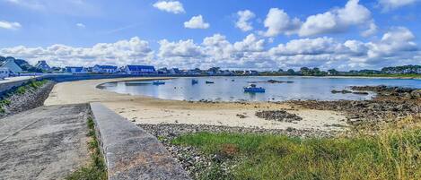 A coastal beach with a curved stone wall, calm water, and boats.