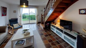 A living room with a sofa, a coffee table with magazines, a TV, and a staircase. - Awesome home in Plouguerneau with house sea view (Plouguerneau)