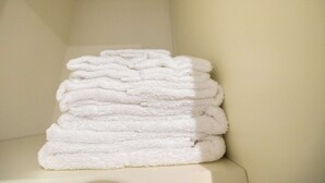 A stack of white towels on a white surface in a room with plain walls.