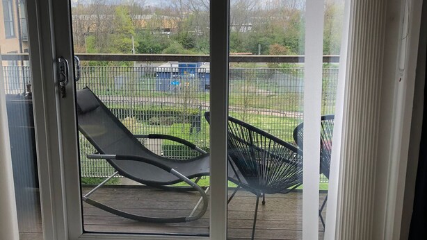 A room with a sliding glass door leading to an outdoor deck with two black lounge chairs.