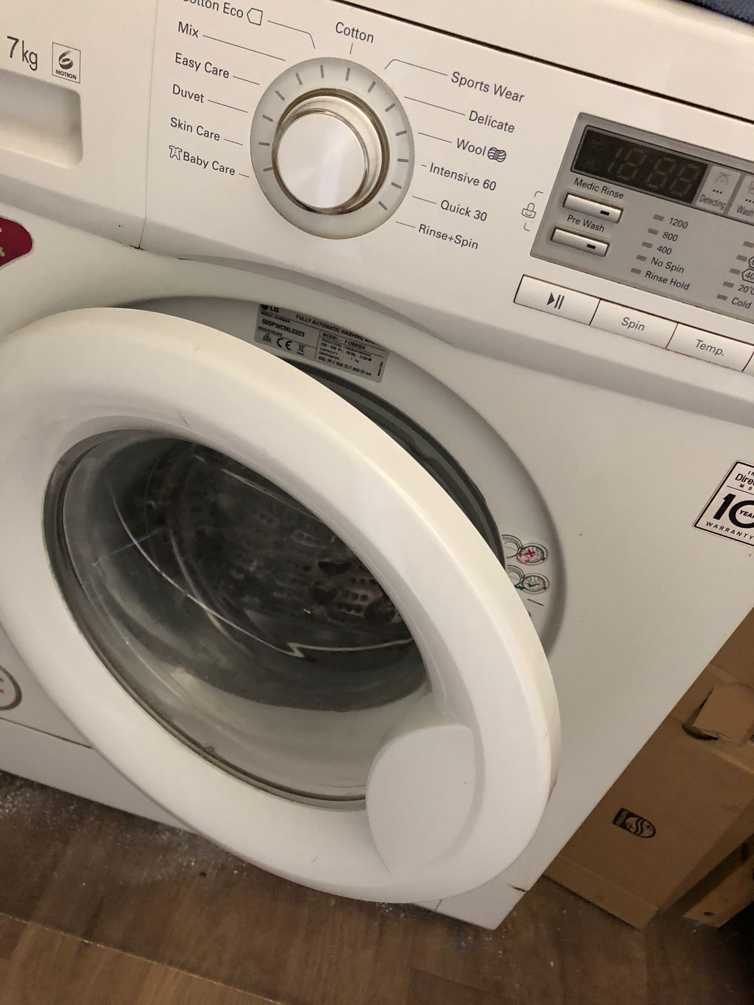 A front view of a front-loading washing machine with a control panel, including a dial for selecting wash cycles and a digital display.