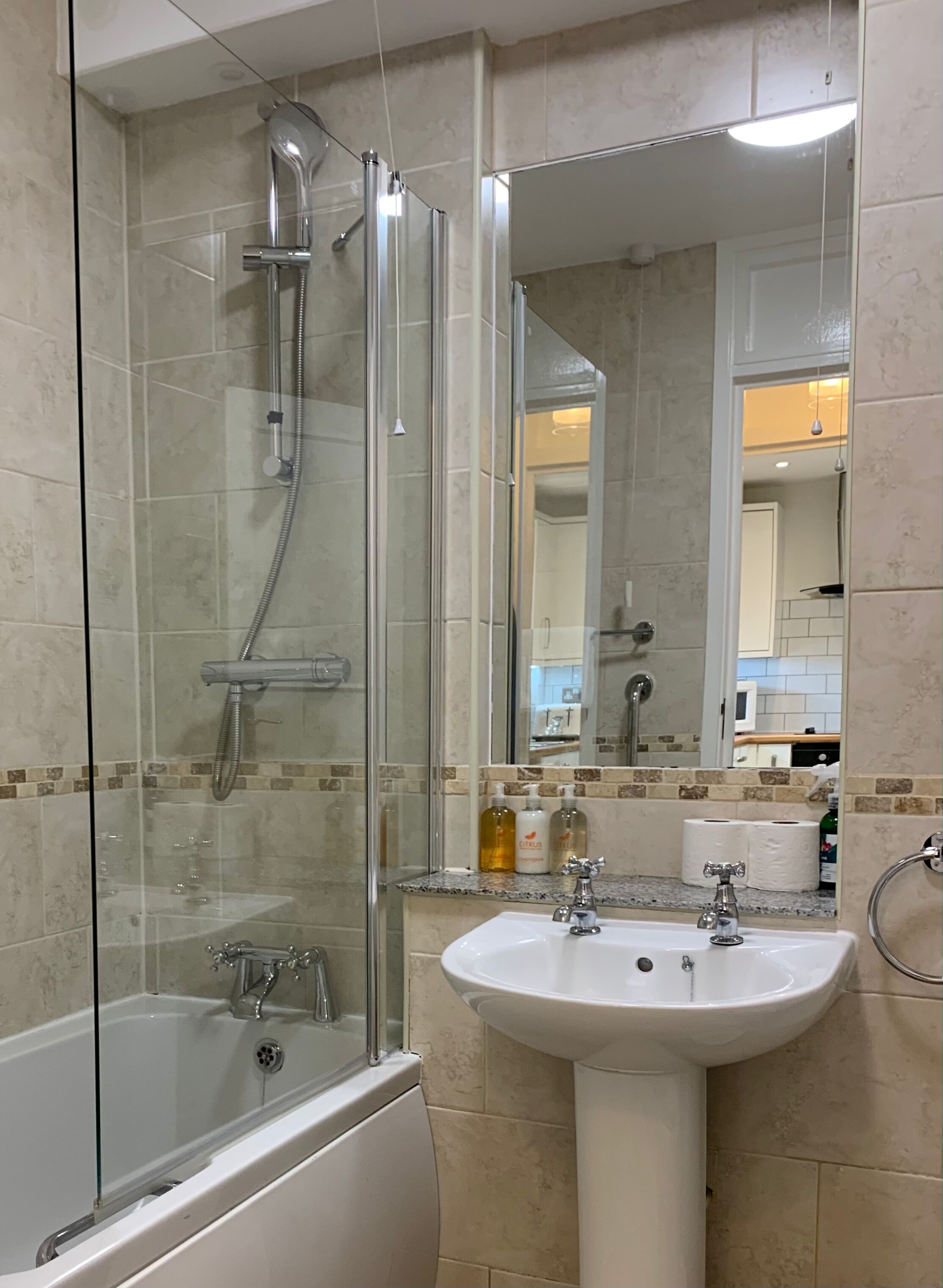 A modern bathroom with a glass-enclosed shower, a white bathtub, and a pedestal sink.