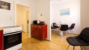 A compact kitchen with a stove, a red cabinet, and a dining area with chairs and a table.