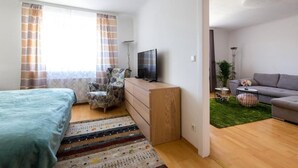 A bedroom with a bed, a TV, a dresser, a chair, a sofa, and a small plant.