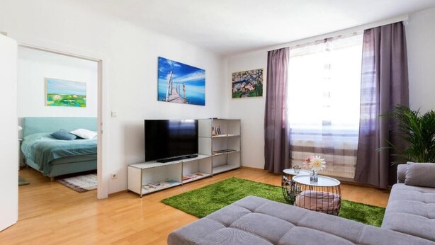 A modern living room with a flat-screen TV, a sofa, a coffee table, and a green rug.
