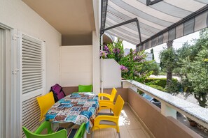 Un balcón con una mesa y sillas, una pared blanca y vista al jardín.