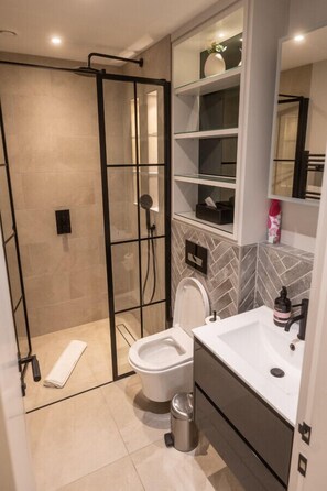 A modern bathroom with a glass-enclosed shower, a white toilet, and a vanity with a mirror.