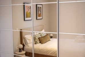 Quarto com cama, travesseiros, mesa de cabeceira e duas quadros na parede.