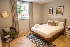 A bedroom with a bed, a chair, a window, and a mirror.