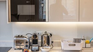 Una cucina con una cappa moderna in acciaio inossidabile, un tostapane, una macchina da caffè e una ciotola con oggetti colorati sul bancone.