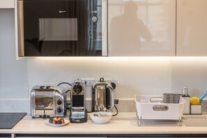 Uma cozinha com um exaustor moderno de aço inoxidável, uma torradeira, uma cafeteira e uma tigela com objetos coloridos na bancada.