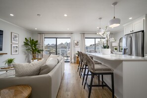 Eine moderne Küche mit Kochinsel, ein Essbereich mit Barhocker und ein Wohnzimmer mit Sofa und Couchtisch.