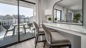 A modern balcony with a glass door, a dining table with chairs, a white console table, and a large mirror. - Two bedroom, 2 bath with pool, newly renovated in 2024! (Ocean City)