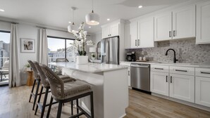 A modern kitchen with white cabinetry, a stainless steel refrigerator, and a central island with bar stools. - Two bedroom, 2 bath with pool, newly renovated in 2024! (Ocean City)