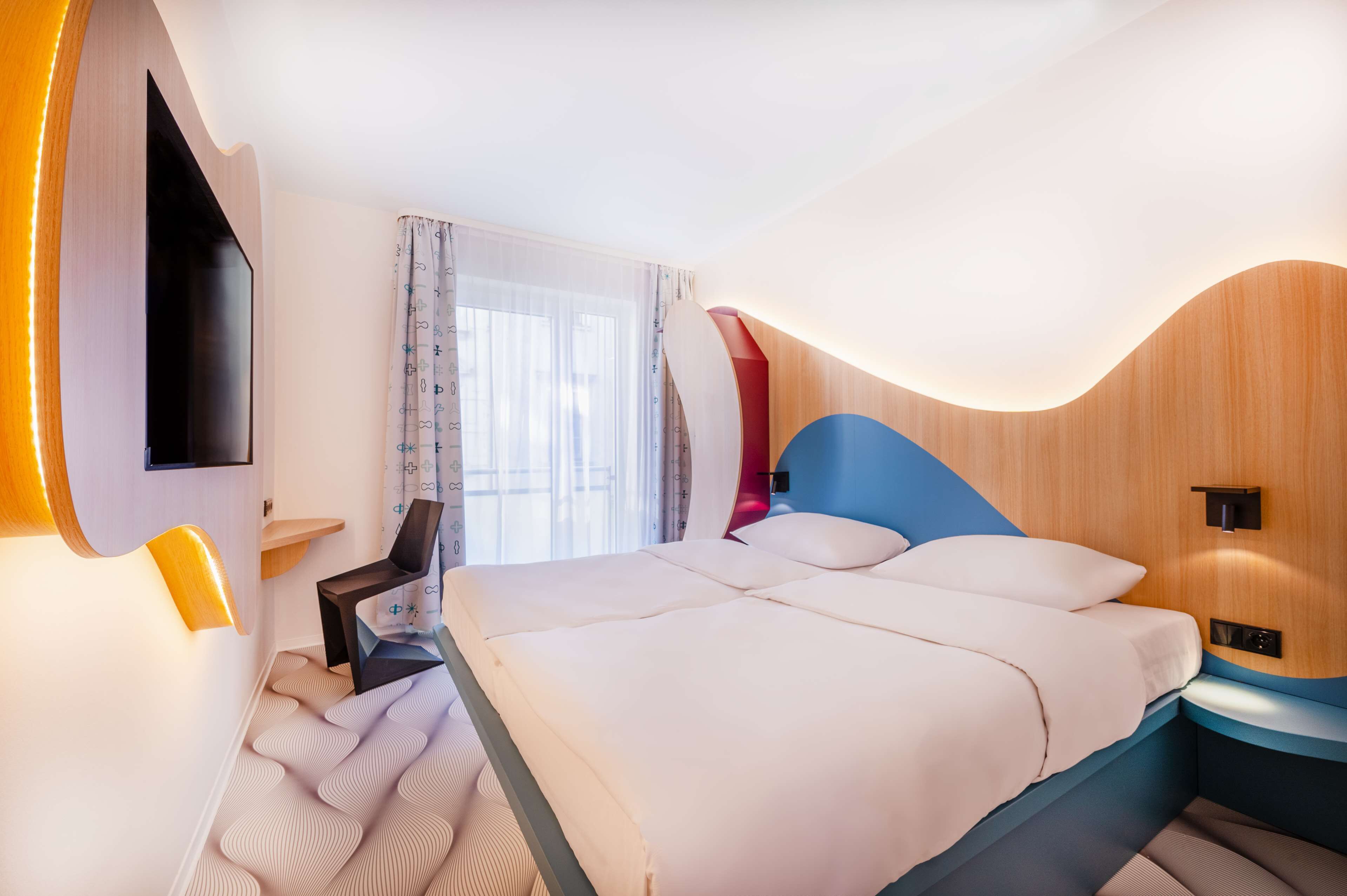 Ein modernes Hotelzimmer mit einem großen Bett, einem Schreibtisch und einem an der Wand befestigten Fernseher.