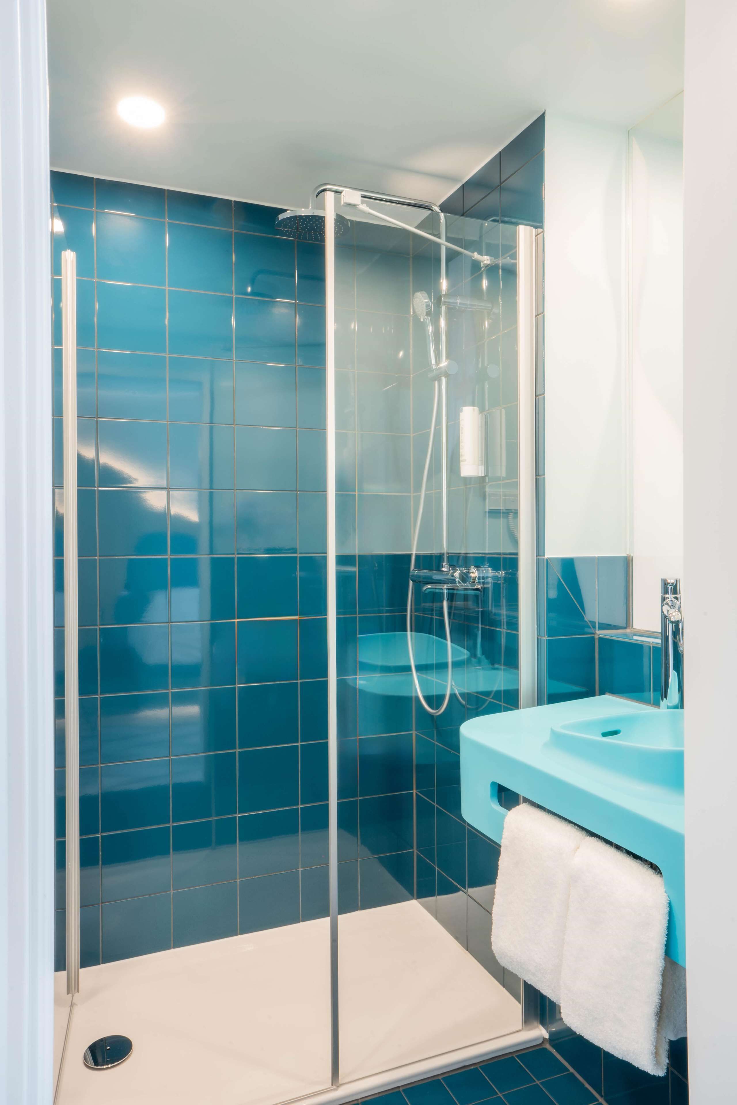 A modern bathroom with a glass-enclosed shower, a blue sink, and a white towel hanging on the wall.