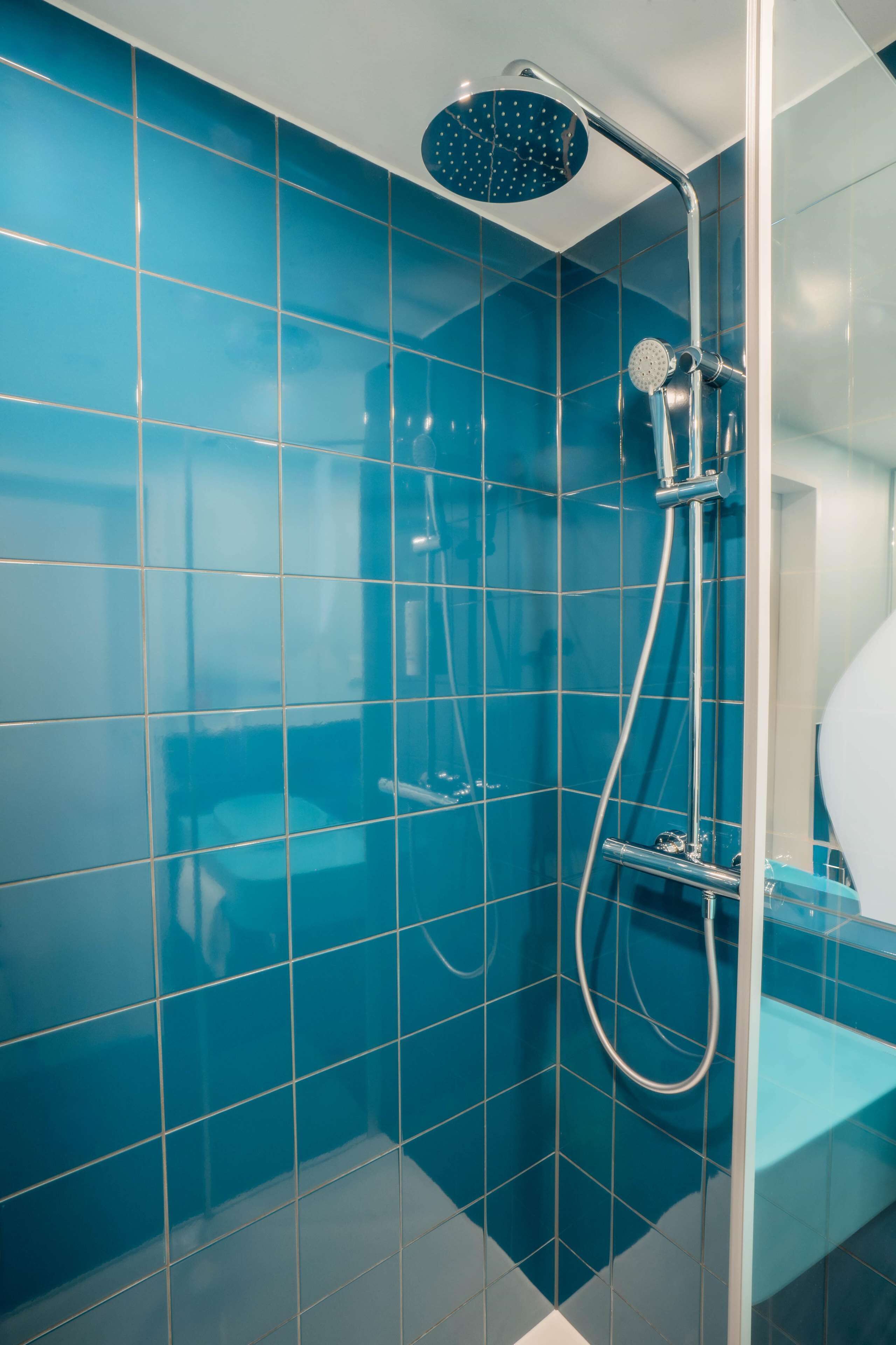 Een badkamer met blauwe tegels, een douche met handdouche en een toilet met glazen cabine.