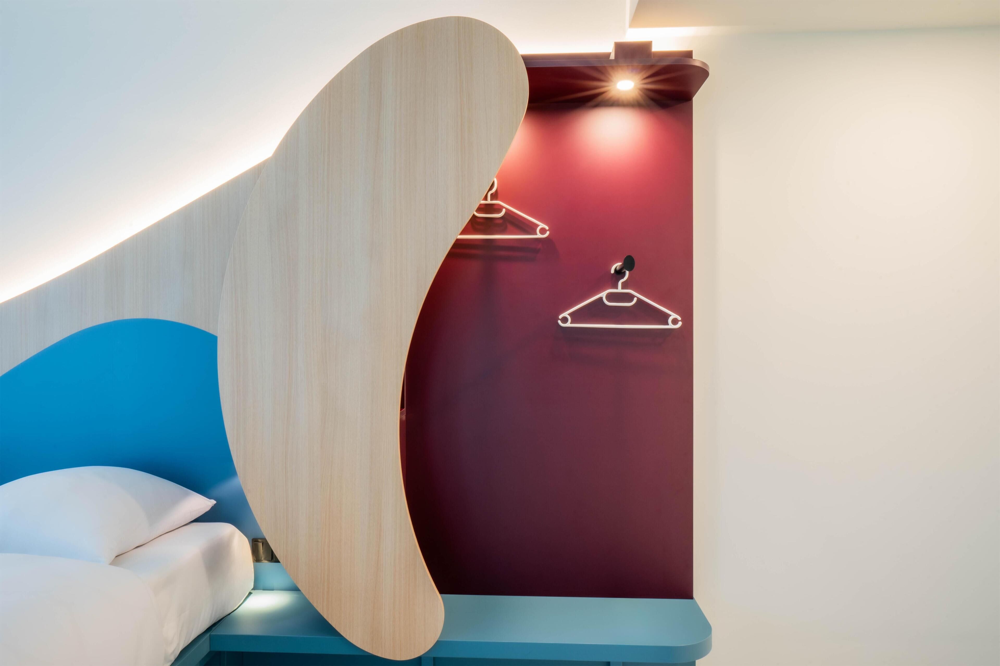 Ein modernes Zimmer mit einem gewölbten Holzkopfteil, einer blauen Akzentwand und einer roten Akzentwand mit einer Leuchte.
