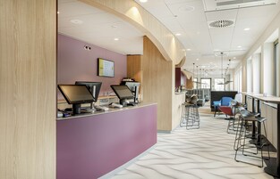 A modern reception area with a curved wooden reception desk, multiple computer monitors, and a seating area with bar stools and chairs.