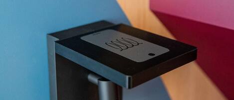 A wall-mounted device with a black base and a rectangular panel, possibly a control panel or sensor, against a wall with a blue and pink color scheme.