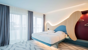 A modern hotel room with a bed, large windows, and a unique wall design. - Prize by Radisson, Dresden Mitte (Dresden)