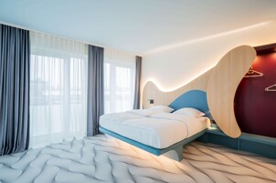 A modern hotel room with a bed, large windows, and a unique wall design.